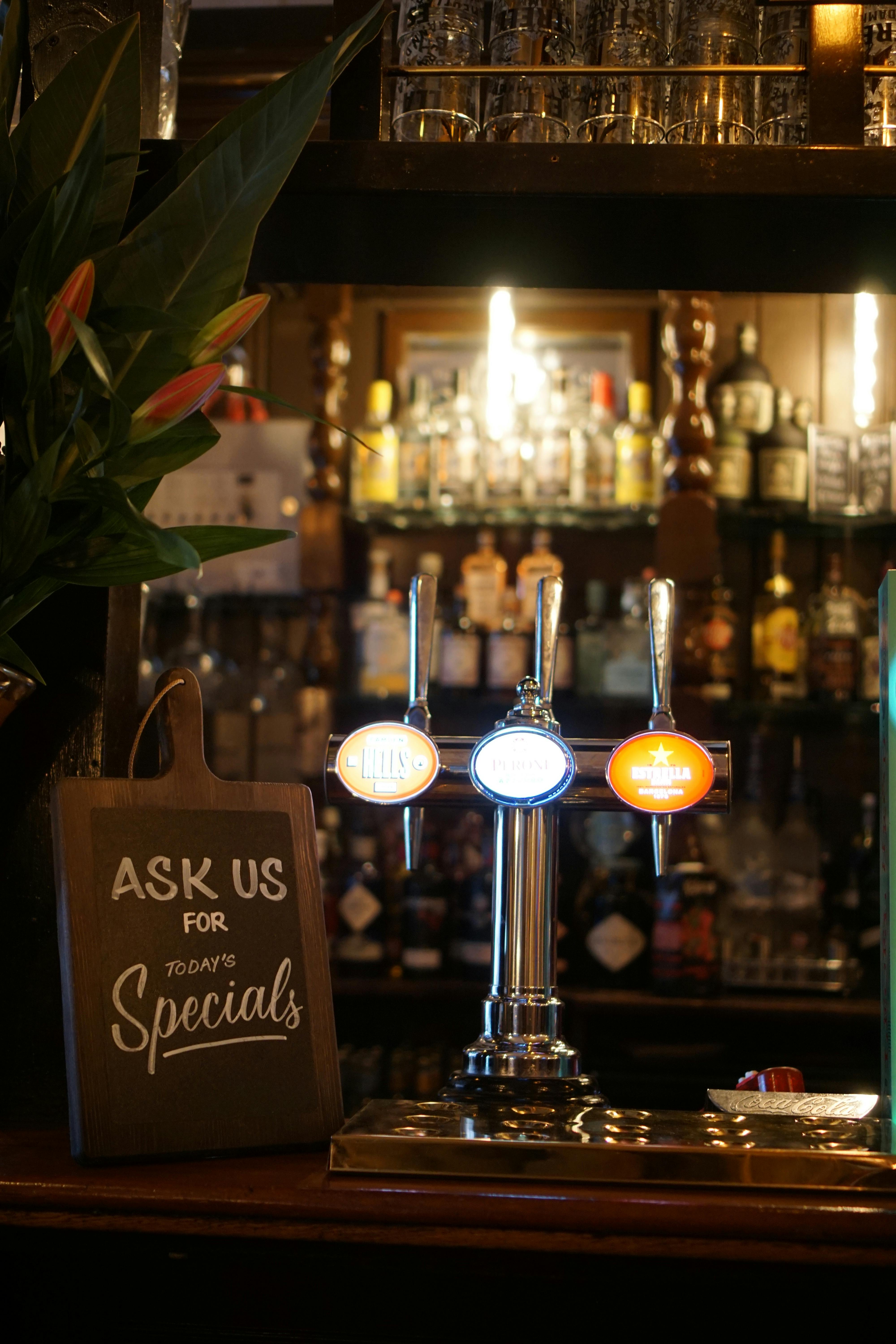 Beer taps on the bar of a traditional pub, with warm lighting and bottles in the background.
